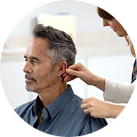 An audiologist fits a hearing aid on a seated man with gray hair in a professional hearing clinic setting, emphasizing personalized hearing care services and expertise.