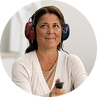 A person undergoing a hearing test holds a response button while wearing red and blue over-ear audiometric headphones in a modern hearing clinic, suggesting professional audiology services for hearing care.