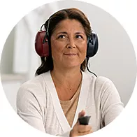 A person undergoing a hearing test holds a response button while wearing red and blue over-ear audiometric headphones in a modern hearing clinic, suggesting professional audiology services for hearing care.
