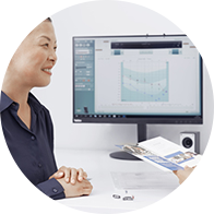 A patient consults with a hearing care specialist in a modern hearing clinic. A hearing test audiogram is displayed on a computer screen, while two hearing aids rest on the table.