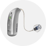 A sleek silver Oticon hearing aid with a slim receiver-in-canal design, green status indicator light, and clear earpiece, set against a plain white circular background.