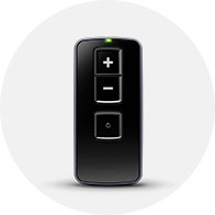 A sleek black remote control for hearing aids features three buttons: volume up (+), volume down (-), and a central multifunction button, with a green indicator light at the top.