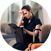 Woman sitting in an airport lounge holding her hand to her head next to luggage.