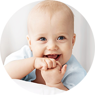 Smiling baby wearing a light blue outfit with a blurred face, sitting indoors.
