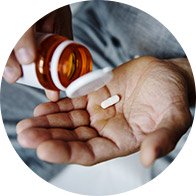 Hand holding a white pill being poured from a brown pill bottle.