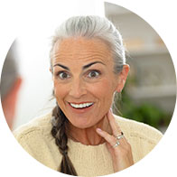 Elderly woman with gray hair and braid leaning forward while holding her hand near her ear.