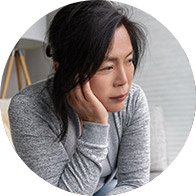 Woman sitting with her head resting on her hand, appearing sad and reflective.