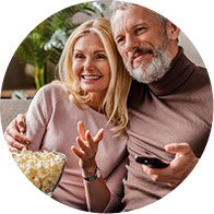 Couple sitting on a sofa enjoying popcorn while holding a remote control, conveying relaxation and quality time.