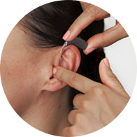 A modern hearing aid is being gently placed behind a woman’s ear by a hand with painted nails, demonstrating proper fitting techniques in a professional hearing care context.