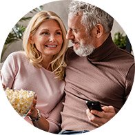 Couple cuddling on a sofa while holding popcorn and a remote control
