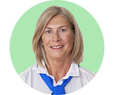 A professional wearing a white collared shirt paired with a blue scarf stands against a solid light green background, possibly representing an audiologist or hearing care specialist from Audika. No text is visible.