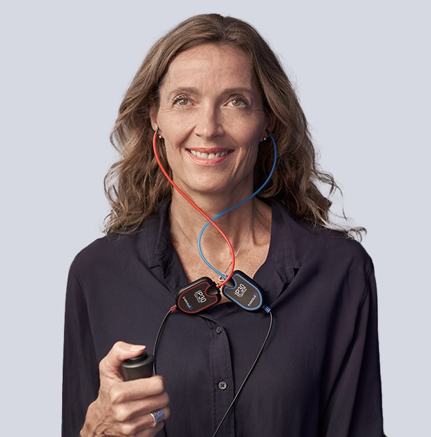 A person is demonstrating a diagnostic hearing test device featuring red and blue earpieces connected to labeled modules (’R’ and ’L’). They are holding a black remote control. Neutral background.