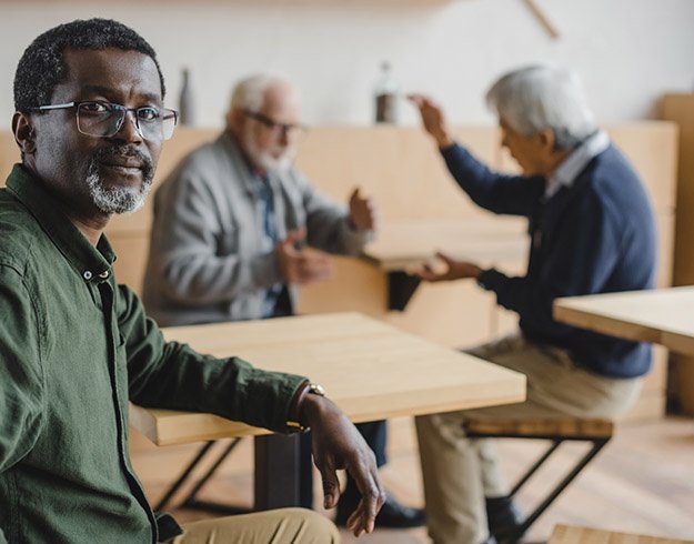 Man feeling excluded while two other men engage in a conversation at a café.