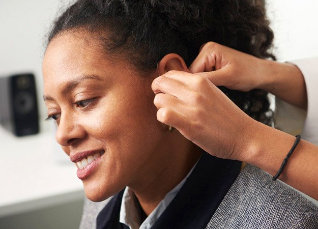 Woman receiving assistance with placing a hearing aid behind her ear.