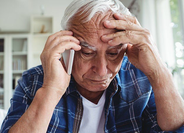 Man holding his head while talking on the phone, appearing distressed.