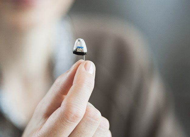 Hand holding a nearly invisible hearing aid designed for discreet hearing support.