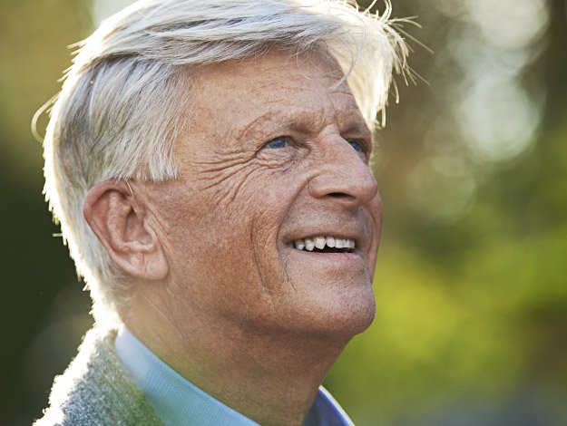 Senior man with gray hair outdoors in a sunlit garden, highlighting his ear.