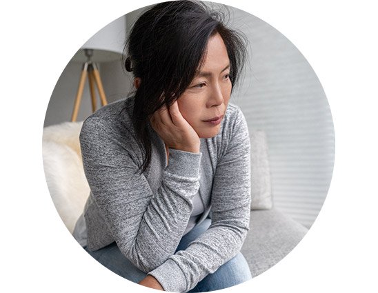 Woman sitting on a couch, appearing thoughtful or concerned, with her face partially obscured.