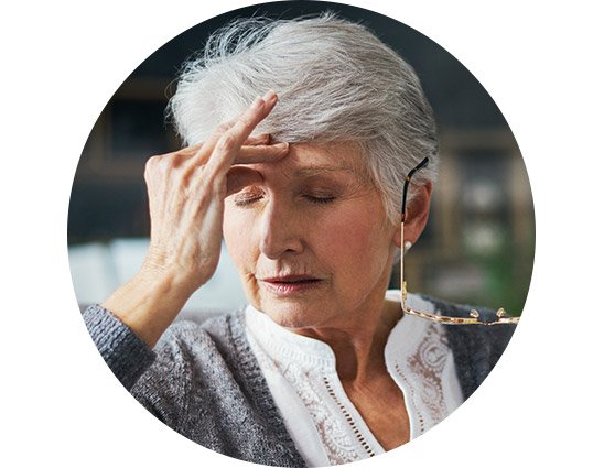 Woman experiencing discomfort while holding her head and glasses.