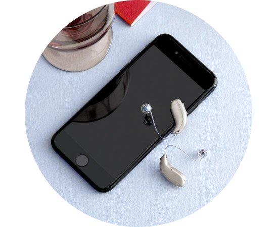 Hearing aids placed next to a smartphone on a light blue surface