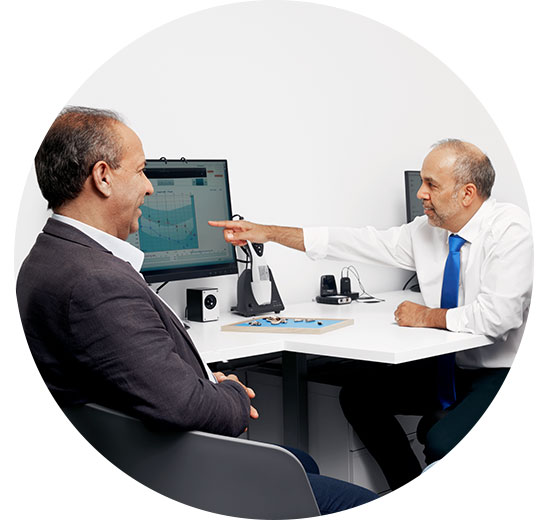 Man consulting an audiologist who is pointing at a screen displaying an audiogram.