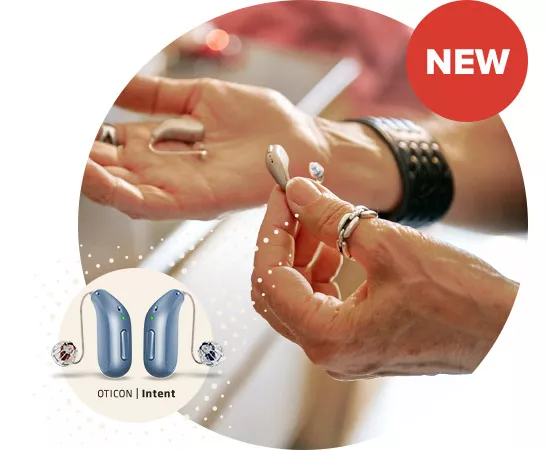 A pair of hands hold and examine sleek, modern hearing aids in a bright indoor setting. The image features Oticon Intent hearing aids, highlighted in a circular callout. ’NEW’ is prominently displayed in a red badge.